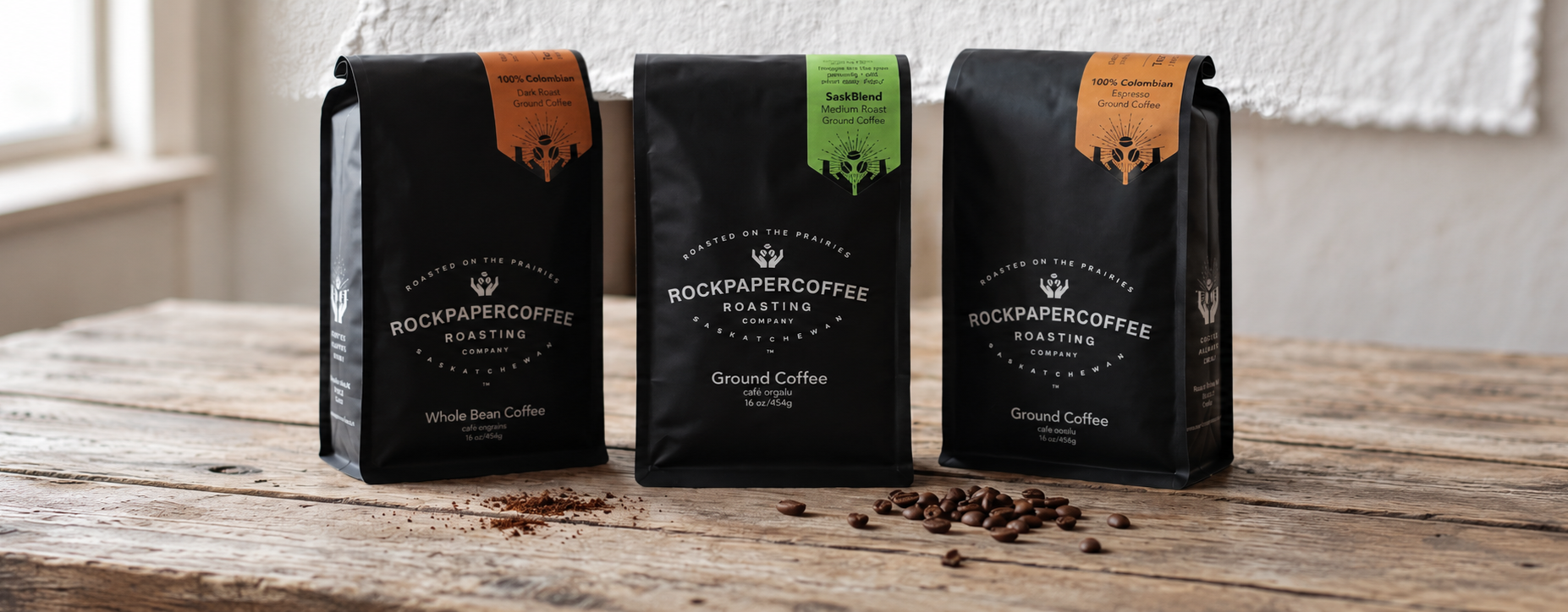 Three Rock Paper Coffee bags on a wooden table: dark roast, medium roast, and Colombian espresso